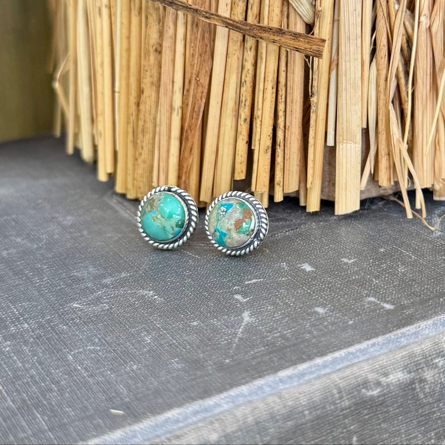 Turquoise stone earrings on a textured surface with a woven basket in the background