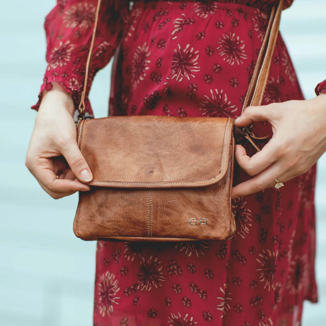 Person holding a brown leather bag with a red floral dress in the background